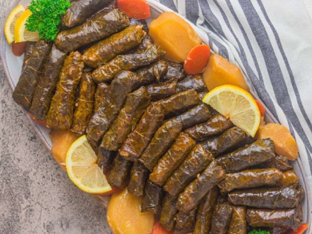 A plate of stuffed grape leaves decorated with lemon wedges and potato and carrot slices