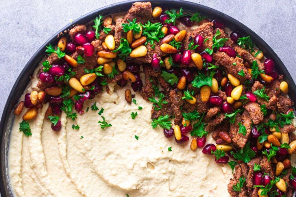 Creamy hummus topped with meat, pine nuts, pomegranate, and chopped parsley