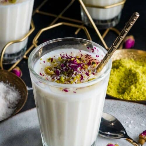 a cup of Middle Eastern sahlab dessert topped with crushed pistachios, shredded coconuts, and dried rose petals