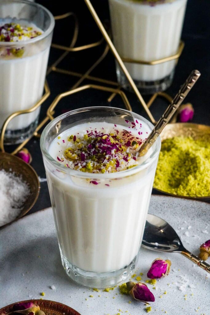 a cup of Middle Eastern sahlab dessert topped with crushed pistachios, shredded coconuts, and dried rose petals