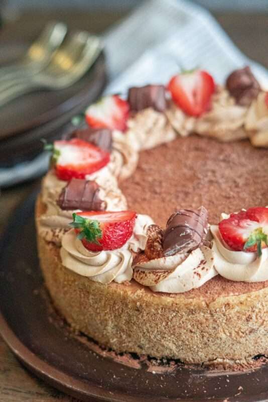 refreshing tiramisu cheesecake made up of hearty creamy coffee-flavored cheesecake filling and yummy crust and topped with a white cocoa whipped cream, chocolate bites, and fresh strawberries