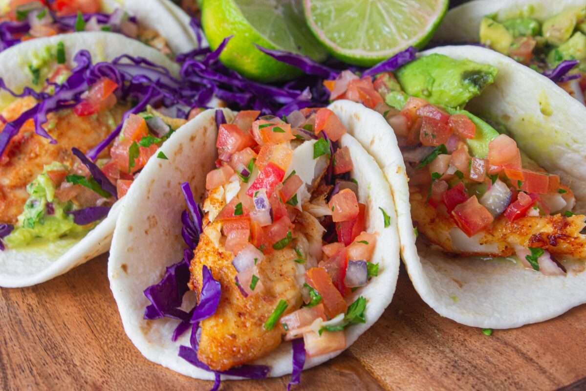 Crispy tortilla bread lies stuffed with fried fish. They also contain shredded cabbage, chopped tomatoes, lemons, and avocados on top.