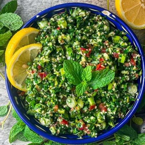 A bowl of tangy, refreshing tabouli salad made of finely chopped parsley, onions, tomatoes, and mint. It is mixed with pre-soaked burghul, a drizzle of olive oil, and lemon juice.