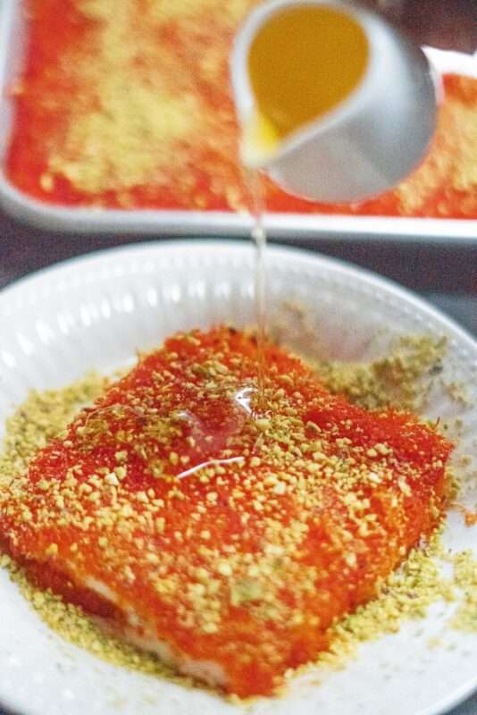 Authentic Palestinian Knafeh garnished with shredded pistachios is being drizzled with aromatic Middle Eastern simple syrup.