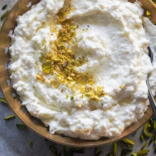 a top shot of ashta served in a plate with crushed pistachios on top and pistachios around the plate