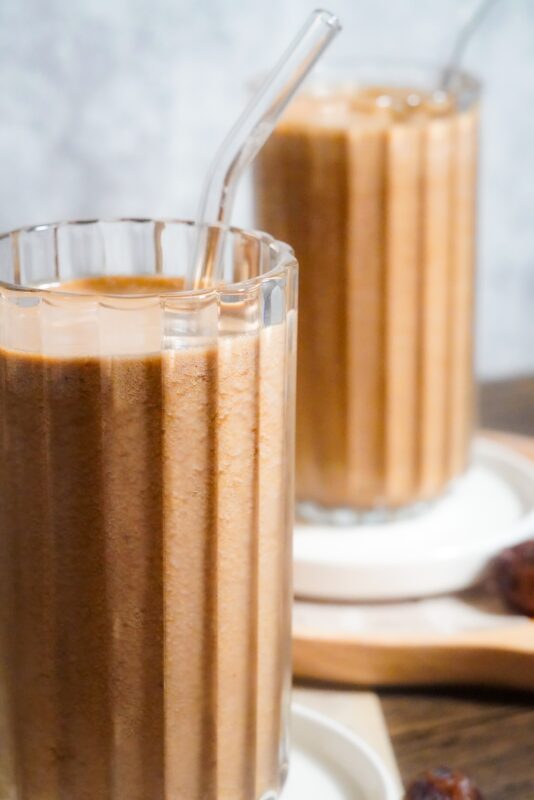two cups of bright brown coffee banana shake with transparent straw in each cup.