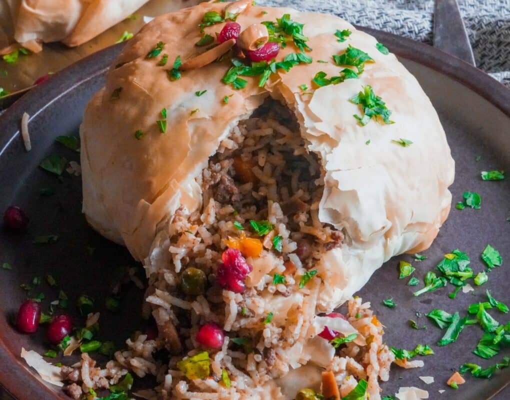 Golden wrapped Ouzi Pocket filled with spiced rice and nuts and garnished with finely chopped fresh parsley and fresh pomegranate seeds.