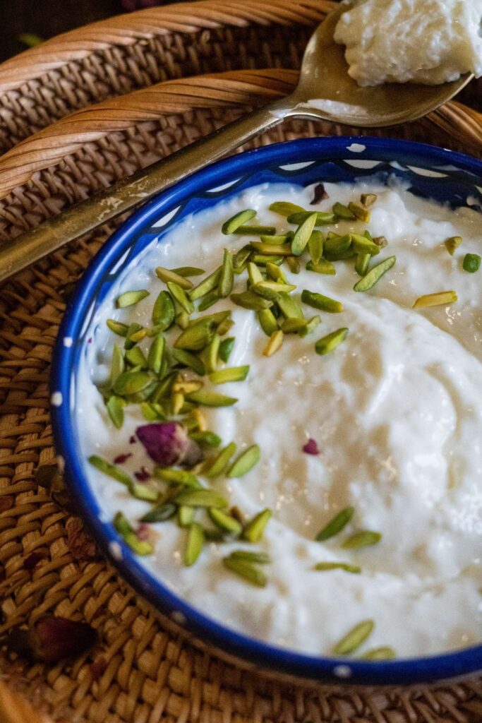 A bowl filled with fresh Ashta topped with thinly sliced pistachios and dried roses.