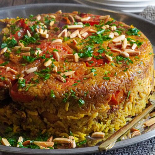 Chicken with rice flipped upside down with nuts and tomatoes on top.