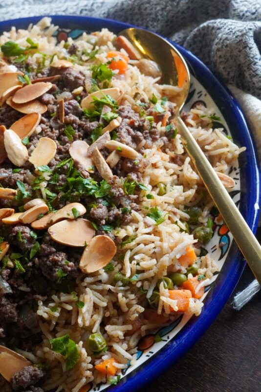 A bright dish packed with spiced rice, peas, and carrots, topped with mouth-watering minced beef, green parsley and toasted nuts.