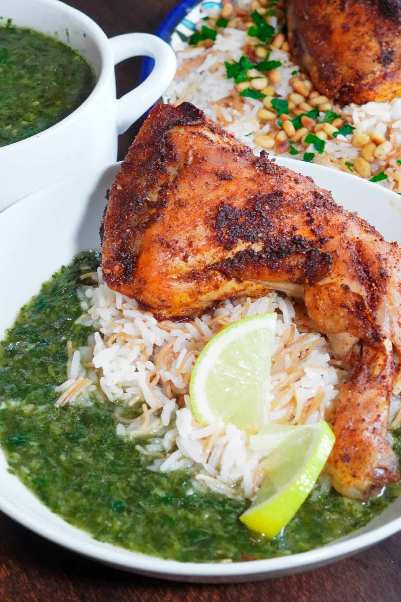 Jews mallow soup in a bowl alongside leg quarters, vermicelli rice, and lemon wedges.