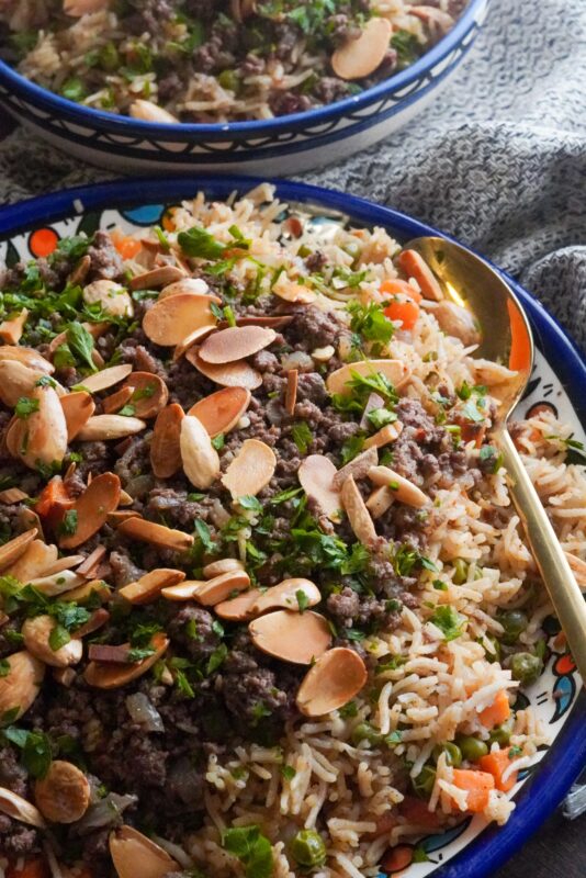 A vibrant platter of well-seasoned rice, peas and carrots garnished with aromatic ground beef, crunchy nuts, and vibrant green parsley.