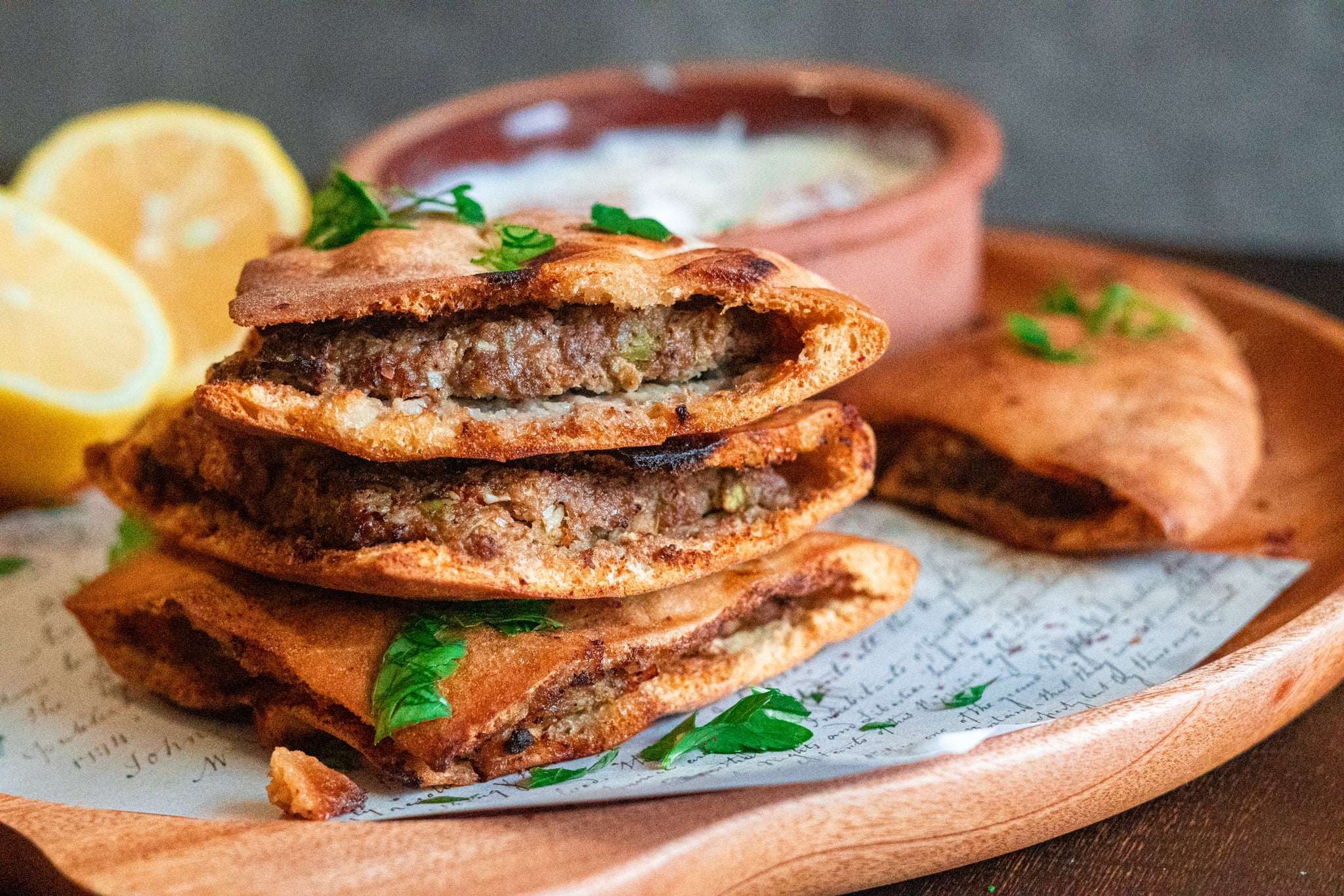 Four meat stuffed pita pockets with a bowl of yogurt and two lemons in the background.