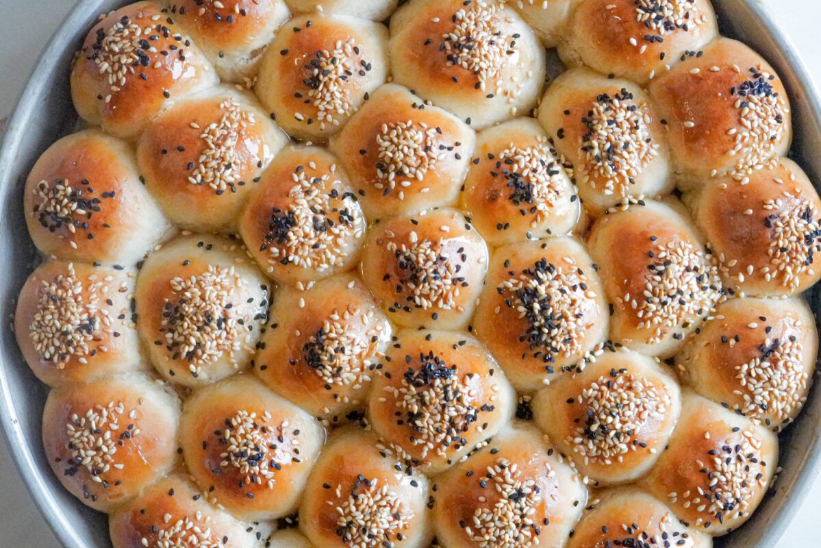 a pan of fluffy honeycomb buns baked to golden perfection topped with sesame seeds and Nigella seeds and drizzled with a lot of honey