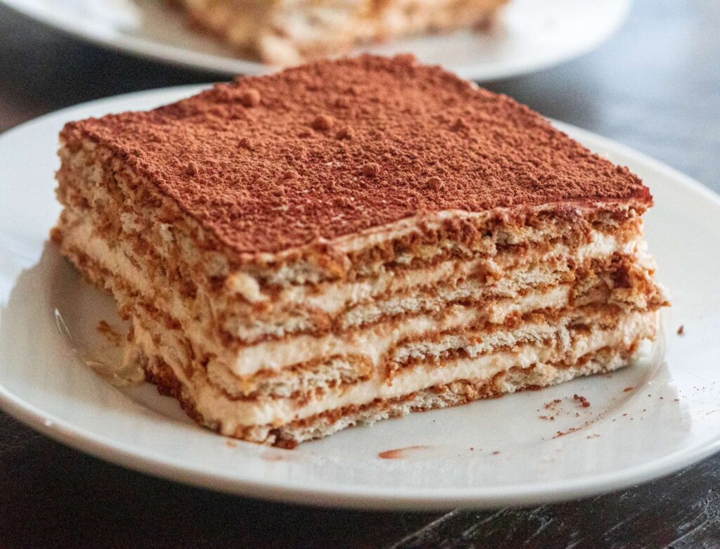 Nescafe Cake decorating a plate with layers of biscuits and cream, topped with cocoa powder.