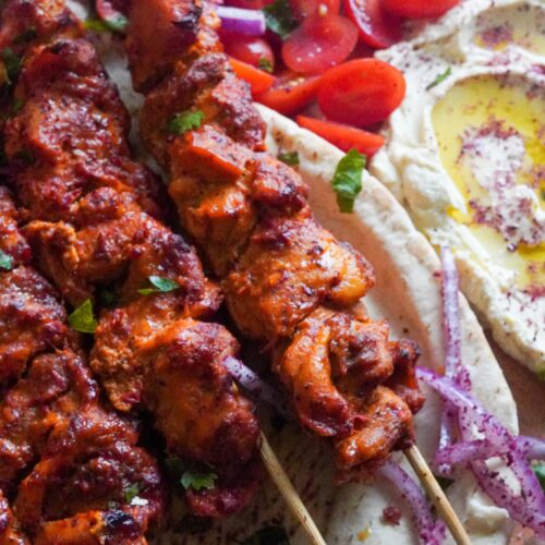 Chicken skewers in a plate with hummus mtabal and cherry tomatoes