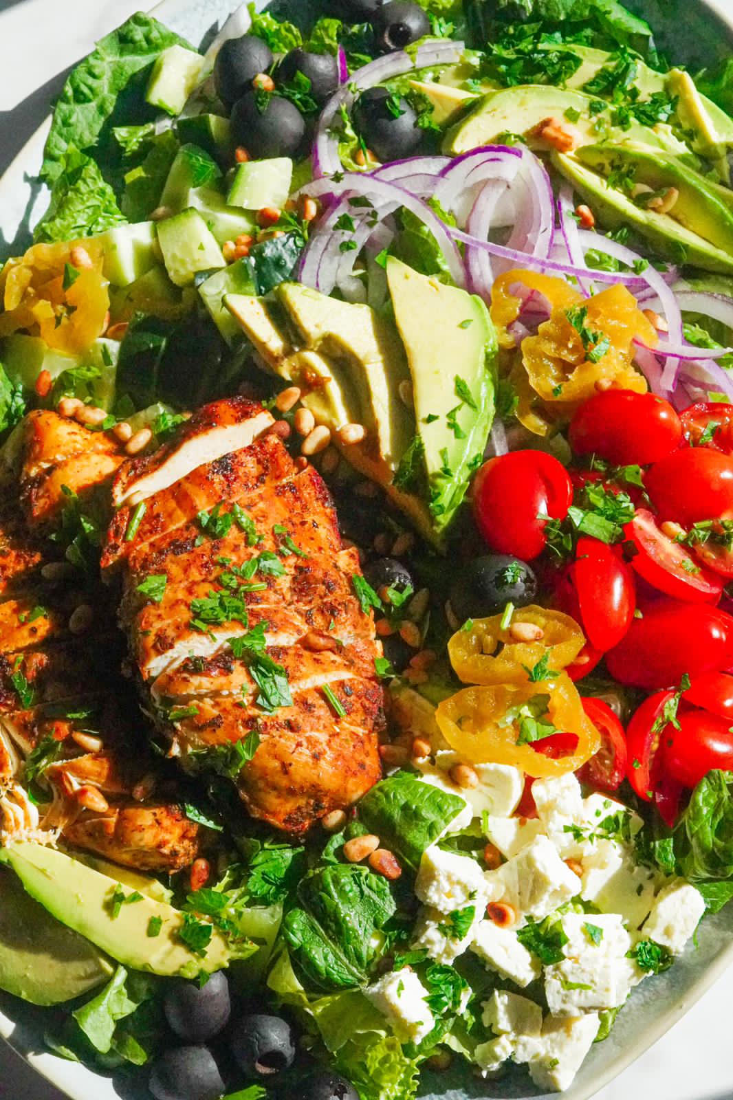 A great bowl of fresh vegetables topped with chicken and avocado slices.