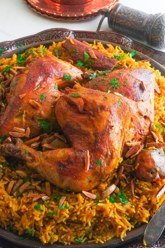 A traditional Saudi Arabian dish of golden-brown cooked chicken pieces over flavorful kabsa rice and served with nuts and almonds.