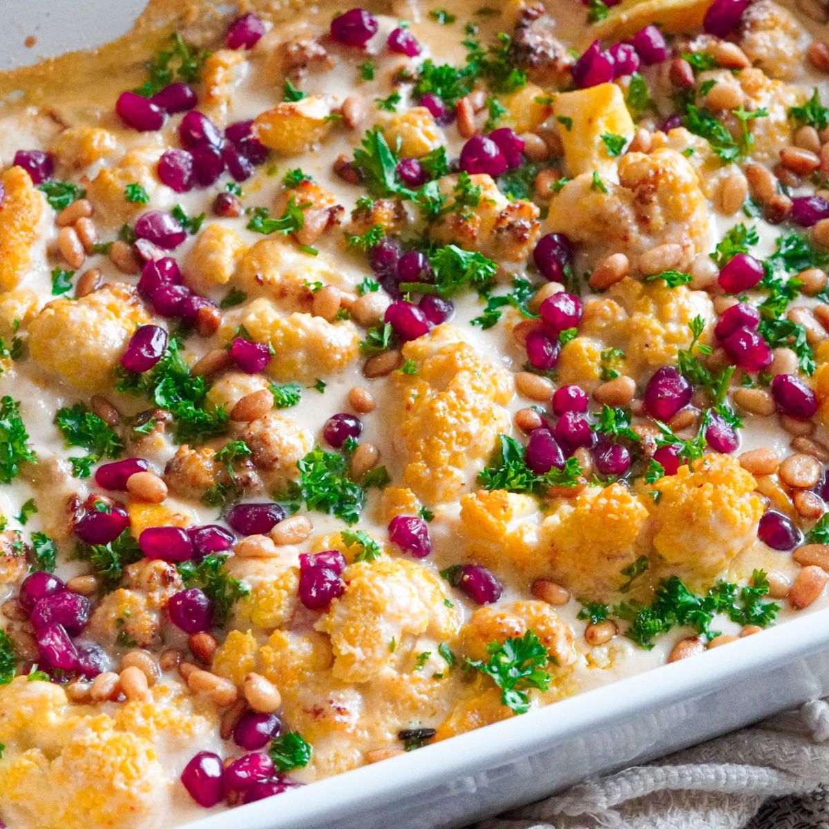 A freshly baked tray of cauliflower garnished with pomegranate seeds, pine nuts and chopped parsley