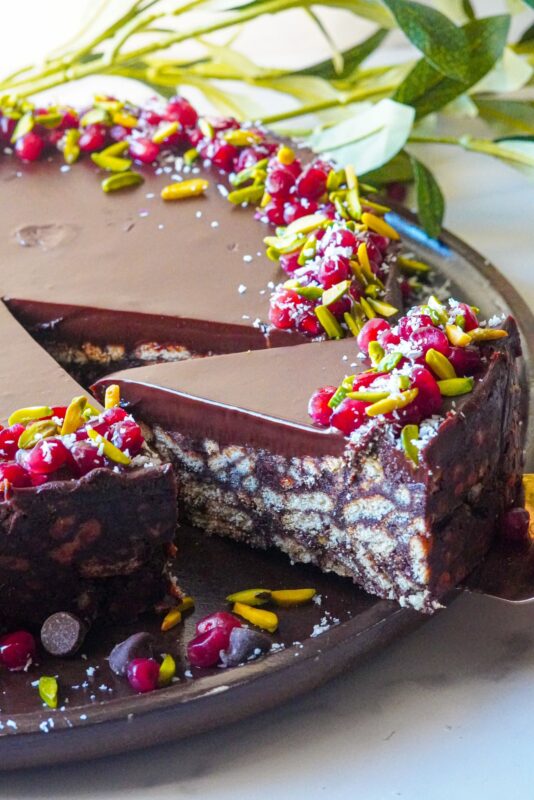 A piece of a lazy cake decorated with pomegranate seeds, shredded pistachios, and coconut shreds