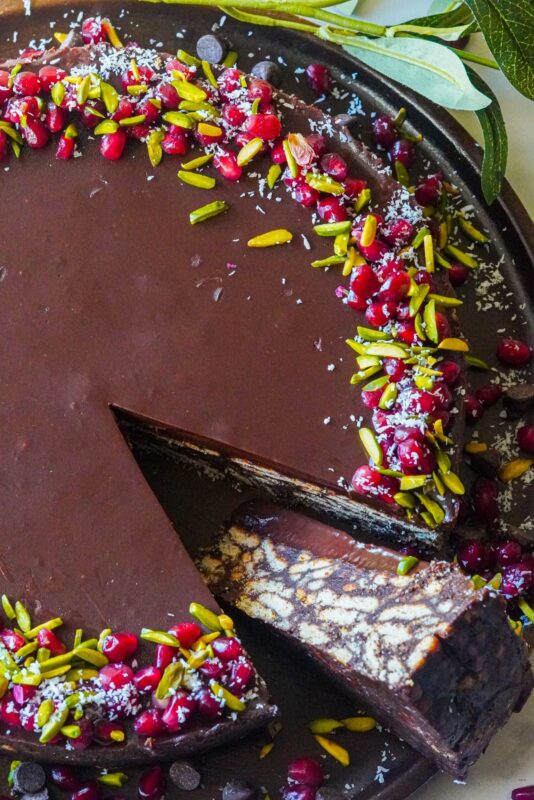 A mosaic figure of biscuits and creamy chocolate lazy cake with sprinkles of chocolate chips pomegranate seeds, shredded coconut and pistachios 