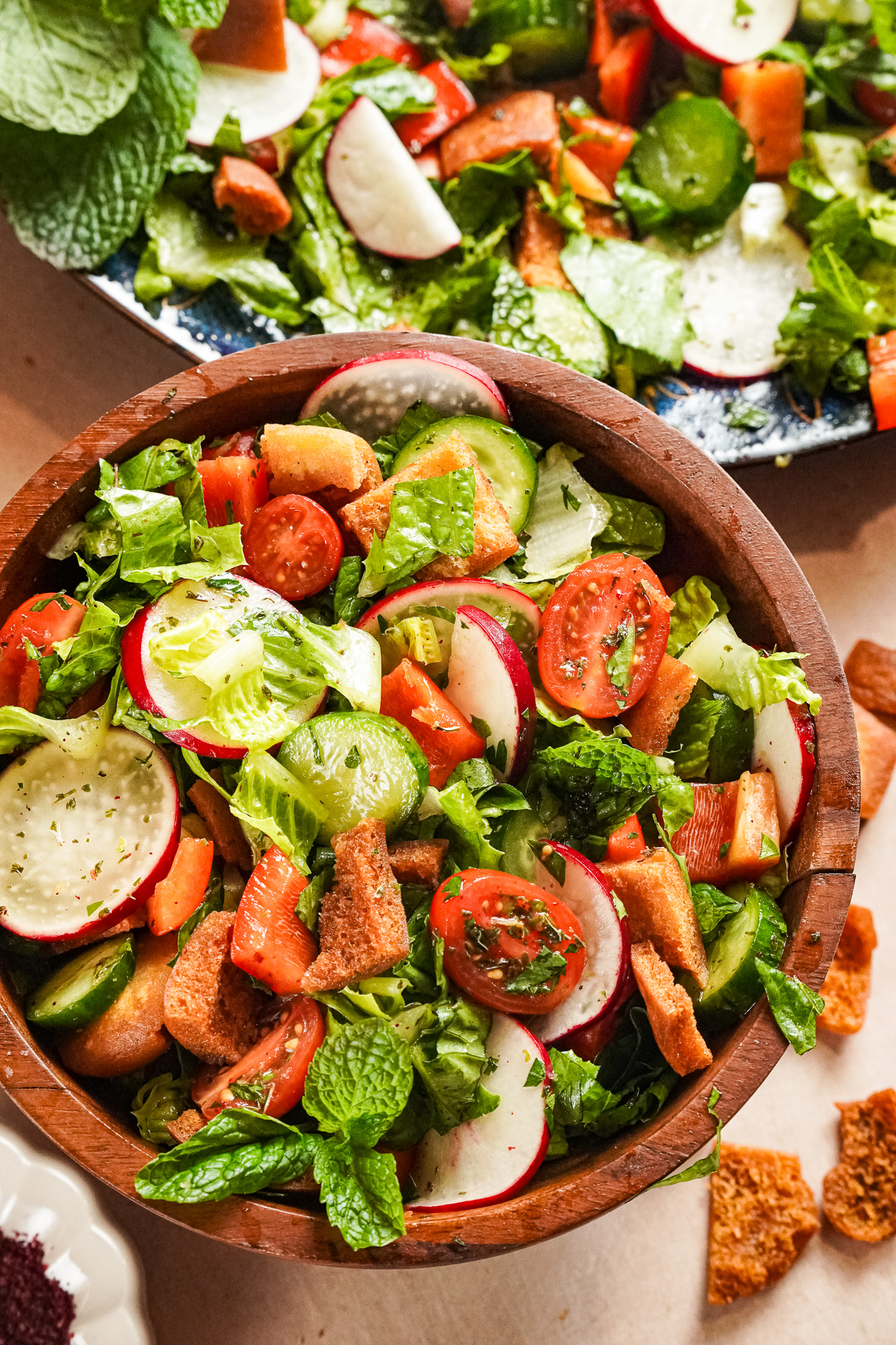 The best fattoush salad containing chopped veggies, lemon wedges and pita chips drizzled with pomegranate molasses