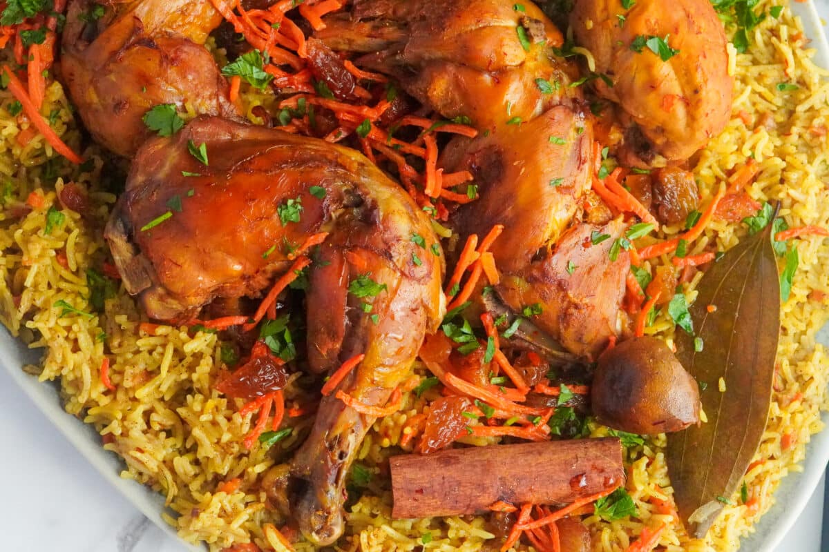 A colorful plate packed with yellow aromatic rice and glossy chicken topped with fresh orange carrots and parsley. 