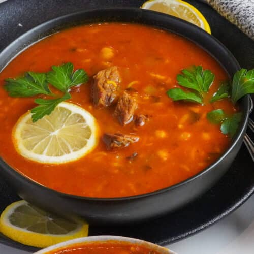 a warm bowl of delicious chickpea and beef soup served with lemon wedges and fresh parsley