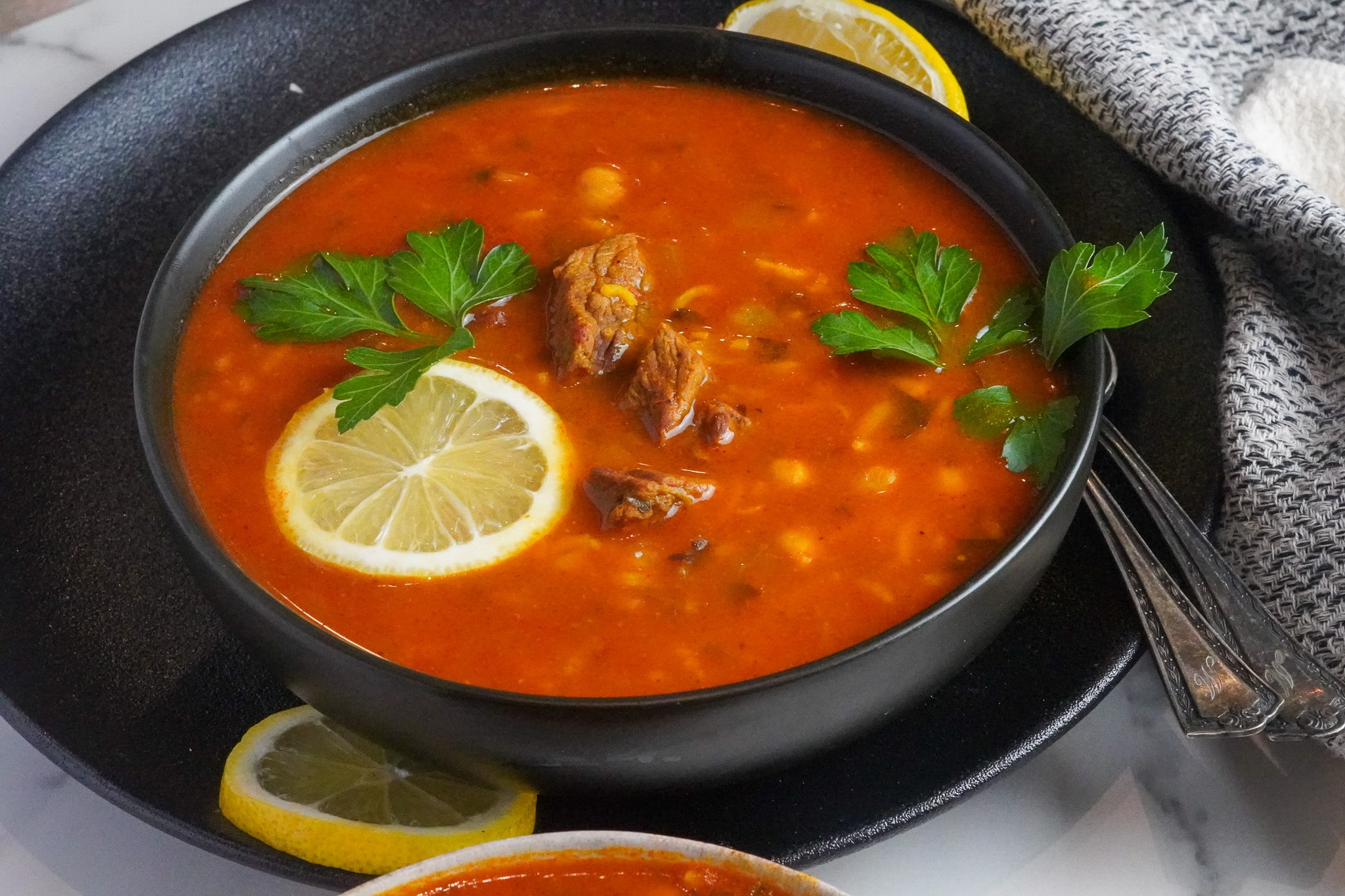 a warm bowl of delicious chickpea and beef soup served with lemon wedges and fresh parsley