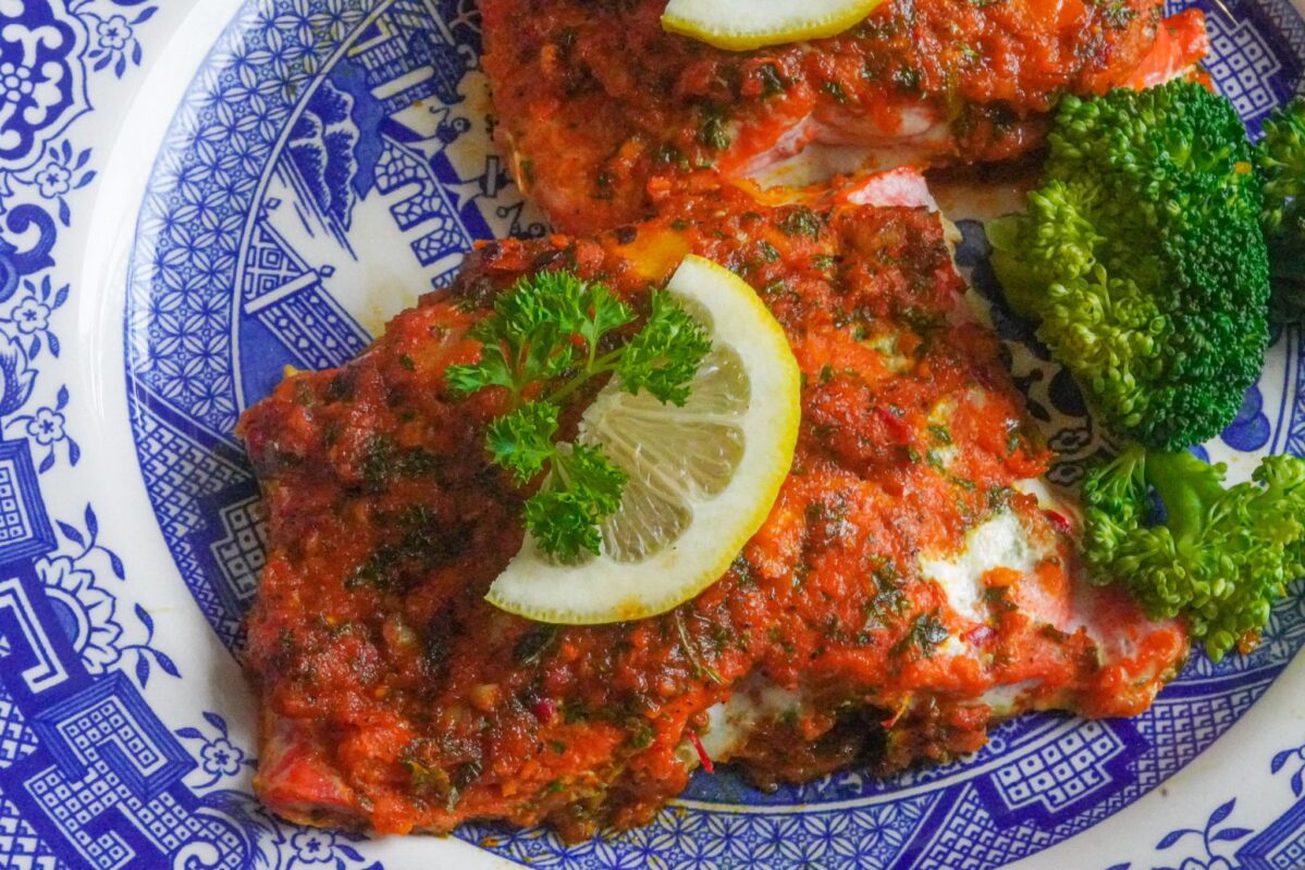 This salmon meal is bursting with flavor and nutrients. It is served with lemon wedge, broccoli, and herbs.