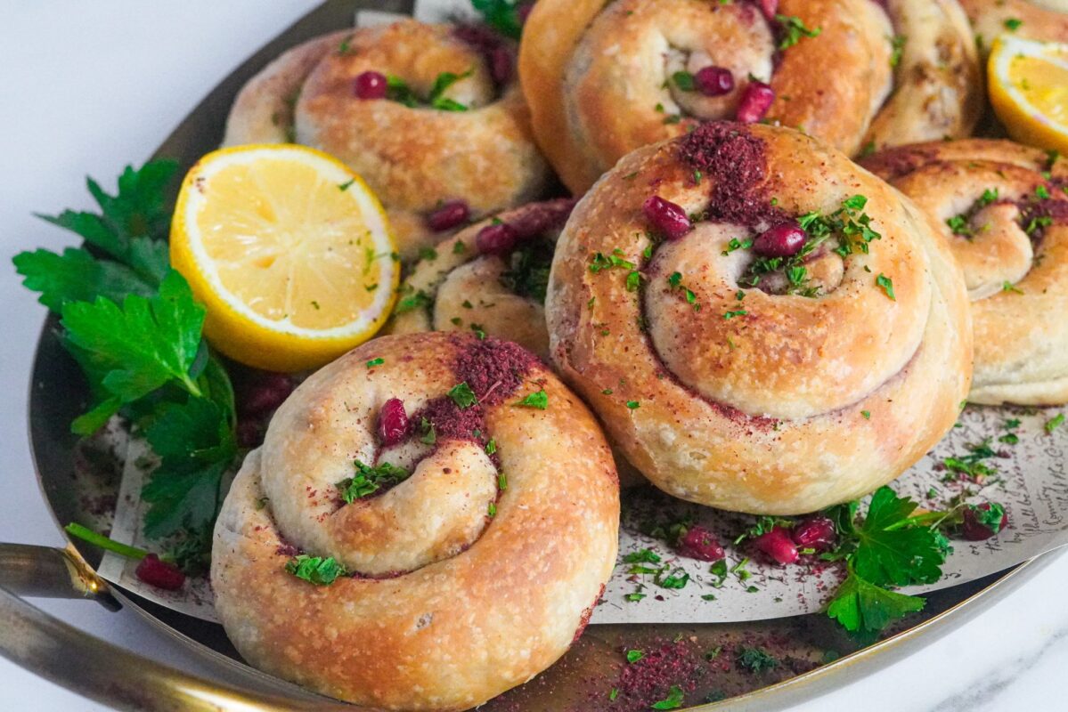 golden spiral meat pies served with lemon halves, arils, and chopped parsley