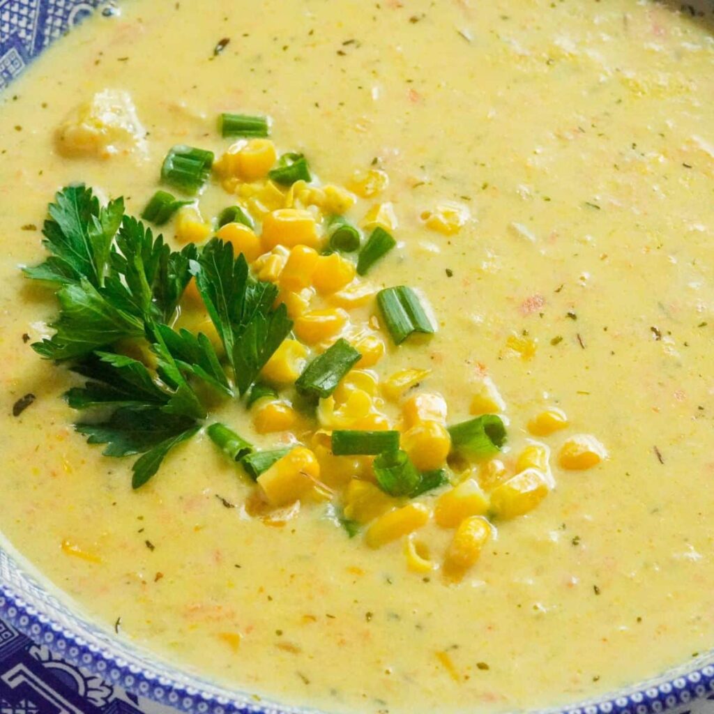 a colorful creamy soup in a blue bowl topped with sweet corn and fresh parsley