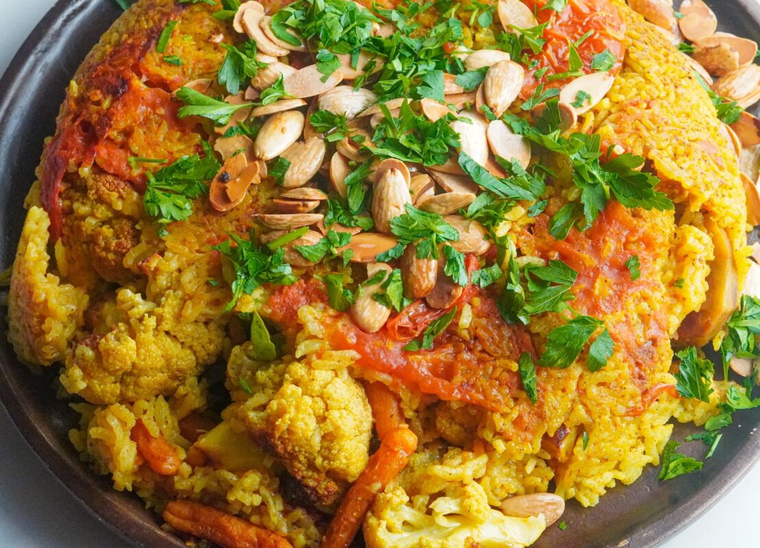 a well-cooked dish of vegetarian makloubeh made of healthy veggies layered with golden rice and topped with some nuts and parsley
