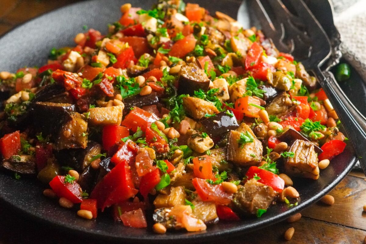 A bowl of eggplant salad with chopped veggies and pine nuts
