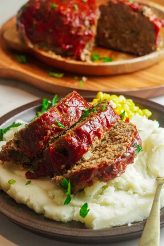 Meatloaf slices on top of mashed potatoes with some corn
