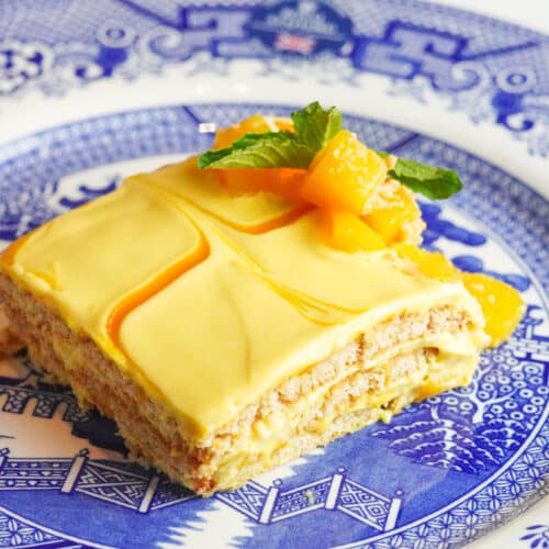 a piece of ice box mango cake served in a blue plate with diced mango and fresh mint leaves on top