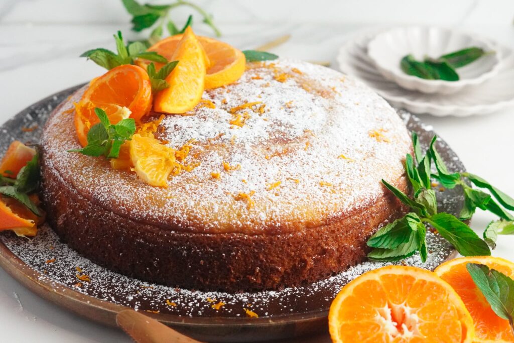 orange cardamom olive oil cake topped with powdered sugar, lemon slices, and fresh mint leaves