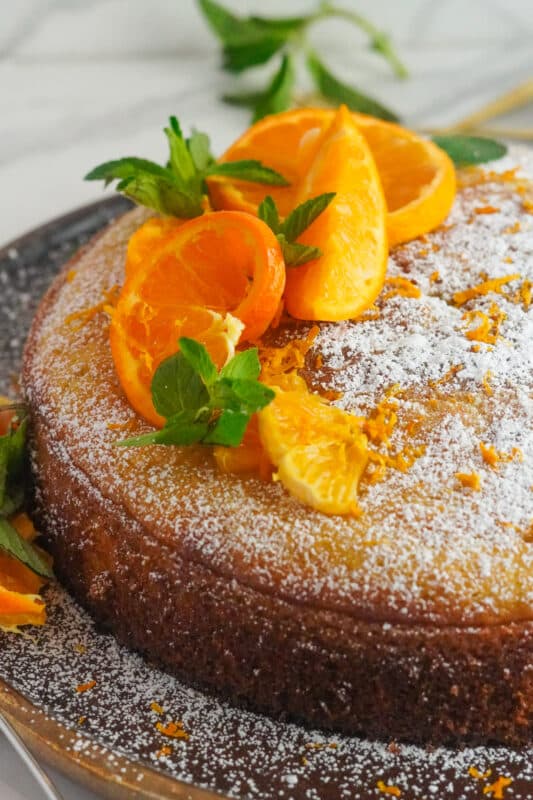 orange cardamom cake topped with powdered sugar, lemon wedges, and mint leaves