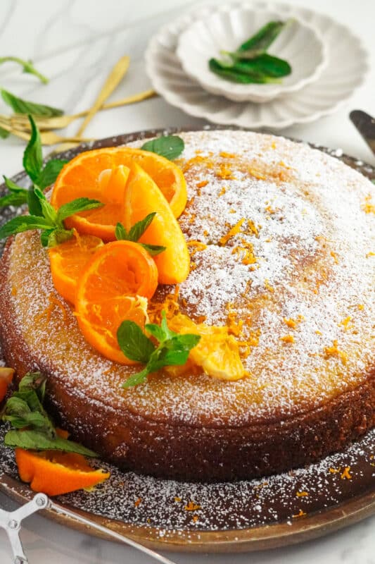 orange flower cake decorated with powdered sugar, lemon zest, and fresh mint leaves