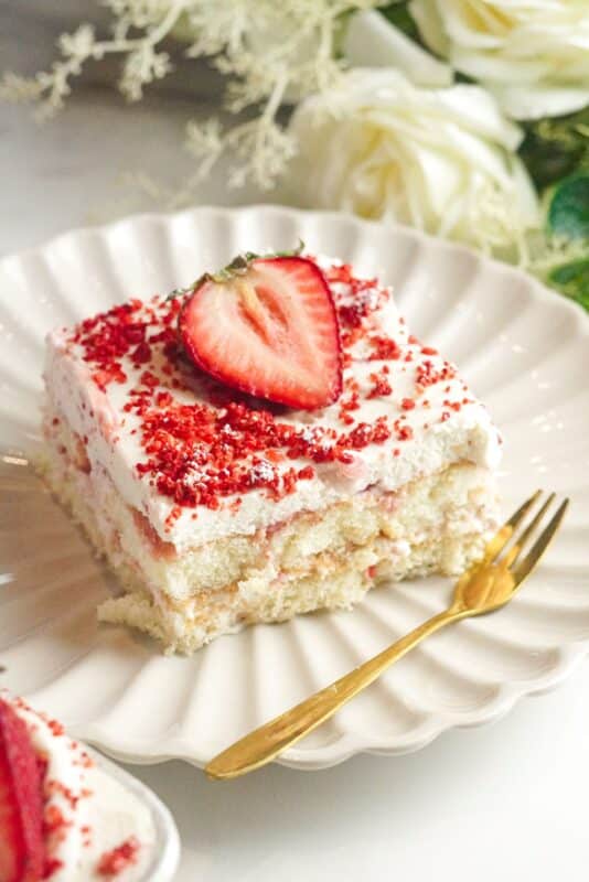 a piece of fresh strawberry tiramisu topped with a layer of vanilla-flavored mascarpone cream, crushed freeze-dried strawberries, and a half of fresh strawberry