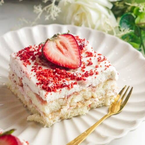 Strawberry tiramisu piece cut in a square shape and served in a white plate with a gold fork