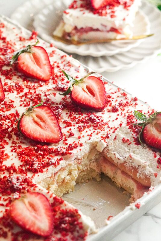 a pan of chilled creamy strawberry tiramisu topped with crushed freeze-dried strawberries and fresh strawberries 