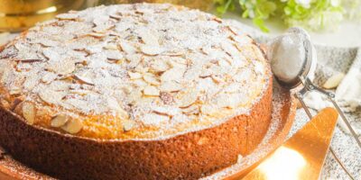 A well decorated almond cake topped with sliced almonds and dusted with powdered sugar