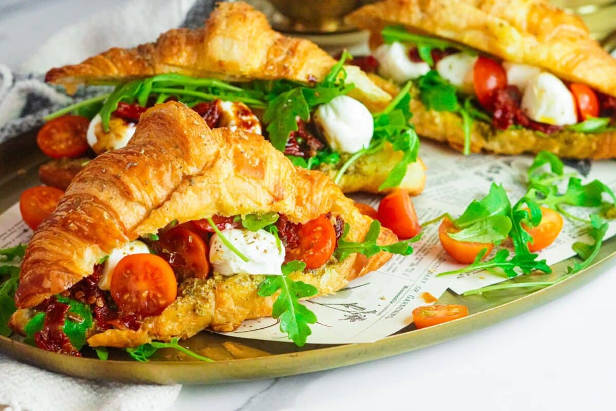 Three buttery croissants stuffed with pesto sauce, sundried and fresh tomatoes, fresh greens, and mozzarella cheese balls.