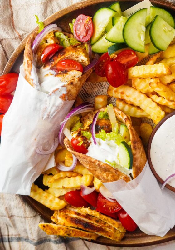 two warm soft sandwiches of chicken with sauce served with French fries, cucumbers, and tomatoes