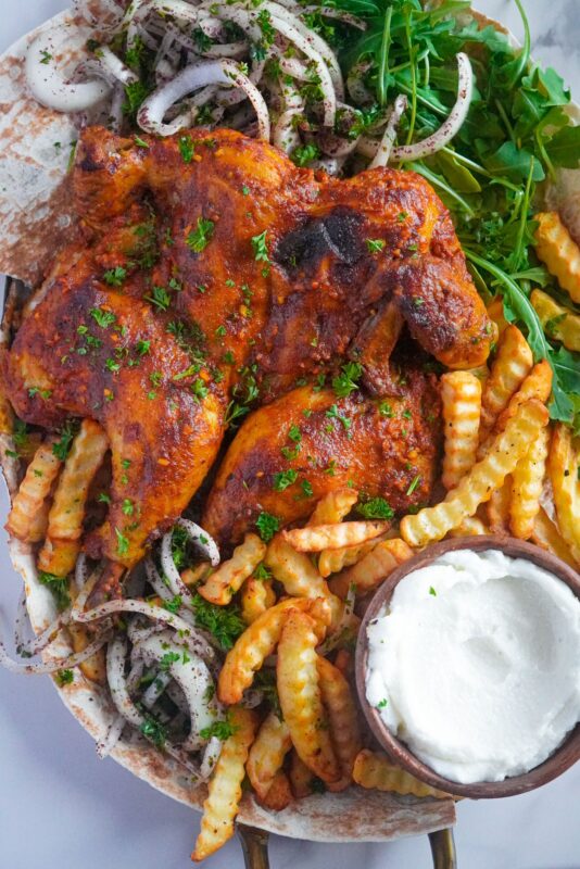 Oven-baked chicken with parsley sprinkles, along with crinkle-cut fries and garlic paste, and sumac onion salad on the side.