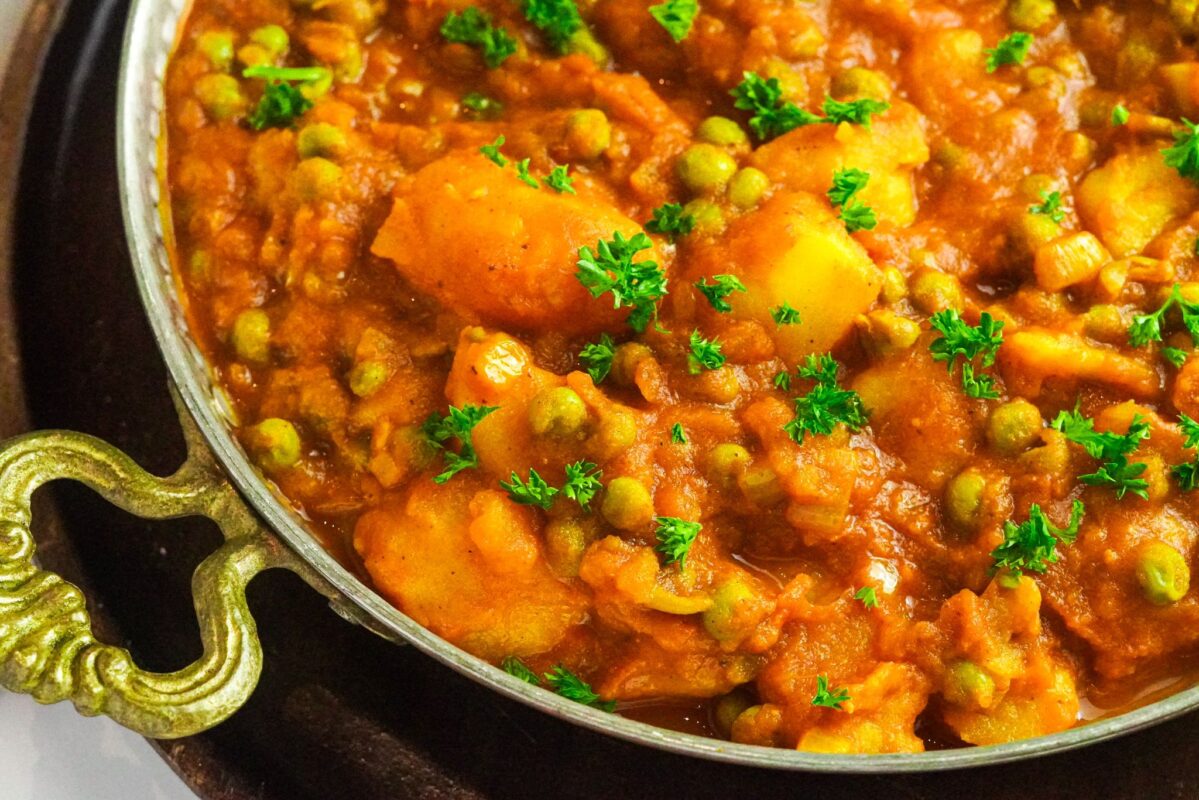 A vibrant curry dish consisting of peas, potatoes, and tomato puree garnished with herbs.