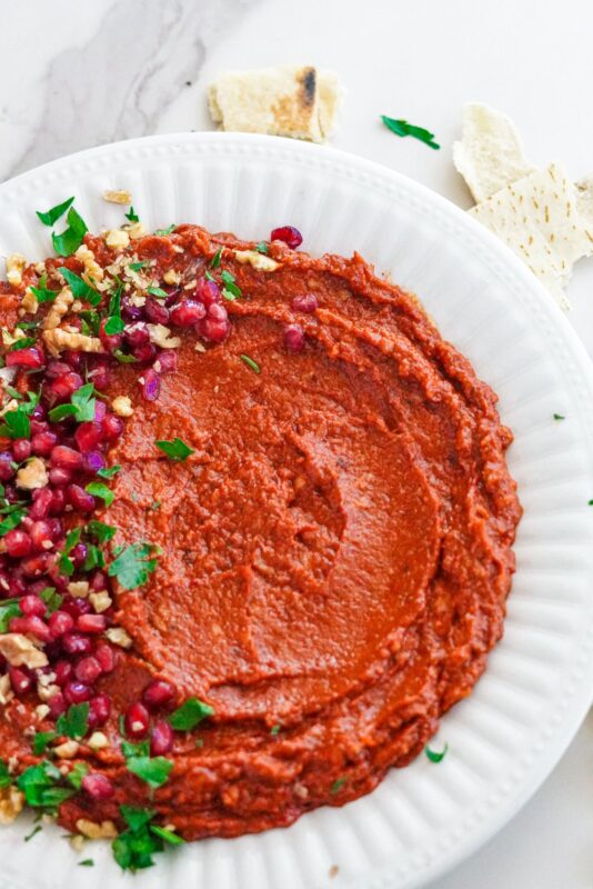 Muhammara dip served with chopped walnuts, pomegranate seeds, and chopped parsley on the top