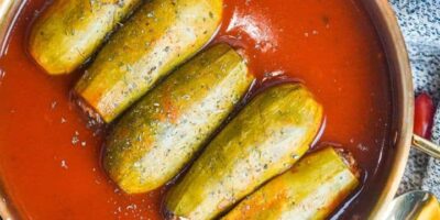 Five zucchinis filled with rice, spices, and lean meat are place horizontally in a big pot containing tomato sauce.
