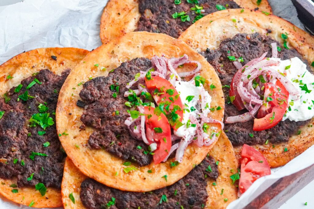 Middle Eastern Inspired Smashed Burger Tacos smothered with a creamy garlic sauce and chopped vegetables